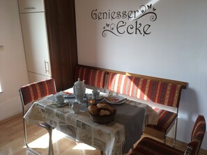 A dining area with a table set for two, a bench, and a wall sign reading "Geniesser Ecke".