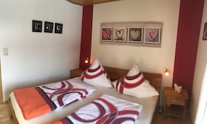 A double bed with a red and white patterned bedspread, two bedside tables with lamps, and a wall with three framed pictures.