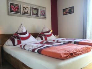 A double bed with a patterned bedspread and two pillows, a wooden headboard, and a wall with framed artwork.