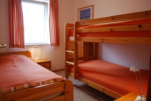 A room with two bunk beds, a bedside table with a lamp, a window with curtains, and a framed picture on the wall. - Comfortable, ground-floor vacation apartment with terrace and garden to make you feel at home. (24217 Schönberger Strand)