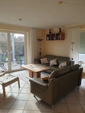 A living room with a sofa, a coffee table, and a floor lamp. There is a sliding glass door leading to an outdoor area. - Comfortable, ground-floor vacation apartment with terrace and garden to make you feel at home. (24217 Schönberger Strand)