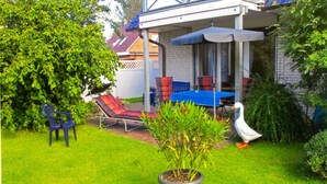 Un jardin avec une pelouse, un parasol bleu, un canard blanc et une plante en pot.