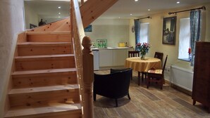 A wooden staircase leading to a dining area with a table and chairs, a black chair, and a radiator. - Boutique Holiday Cottage set in a large and tranquil garden near Durrus (Durrus)