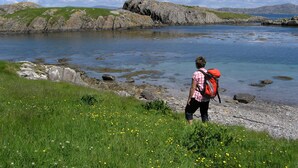 A person standing by a lake with a rocky shoreline and grassy areas. - Boutique Holiday Cottage set in a large and tranquil garden near Durrus (Durrus)