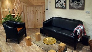 A living room with a black leather sofa, a wooden staircase, and two wall decorations. - Boutique Holiday Cottage set in a large and tranquil garden near Durrus (Durrus)