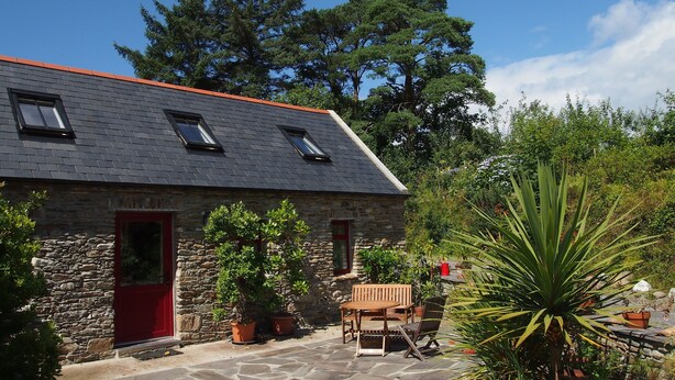 A stone building with a red door, a wooden table and chairs, and potted plants. - Boutique Holiday Cottage set in a large and tranquil garden near Durrus (Durrus)