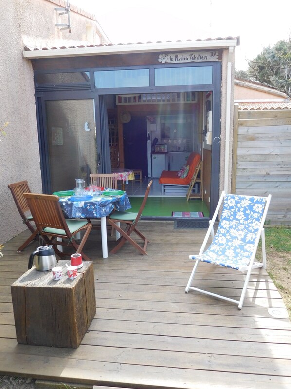 Un patio exterior con una mesa, sillas, una silla plegable y una pequeña zona de terraza.