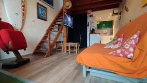 Ein gemütlicher Wohnraum mit einer Couch, einem roten Sessel, einer Holztreppe und einer Küchenzeile.