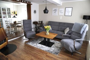 A modern living room with a grey sofa, two armchairs, a wooden coffee table, and a black and white rug.