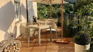 Une terrasse extérieure avec des tables et des chaises en bois, un grand parasol et des plantes en pot.
