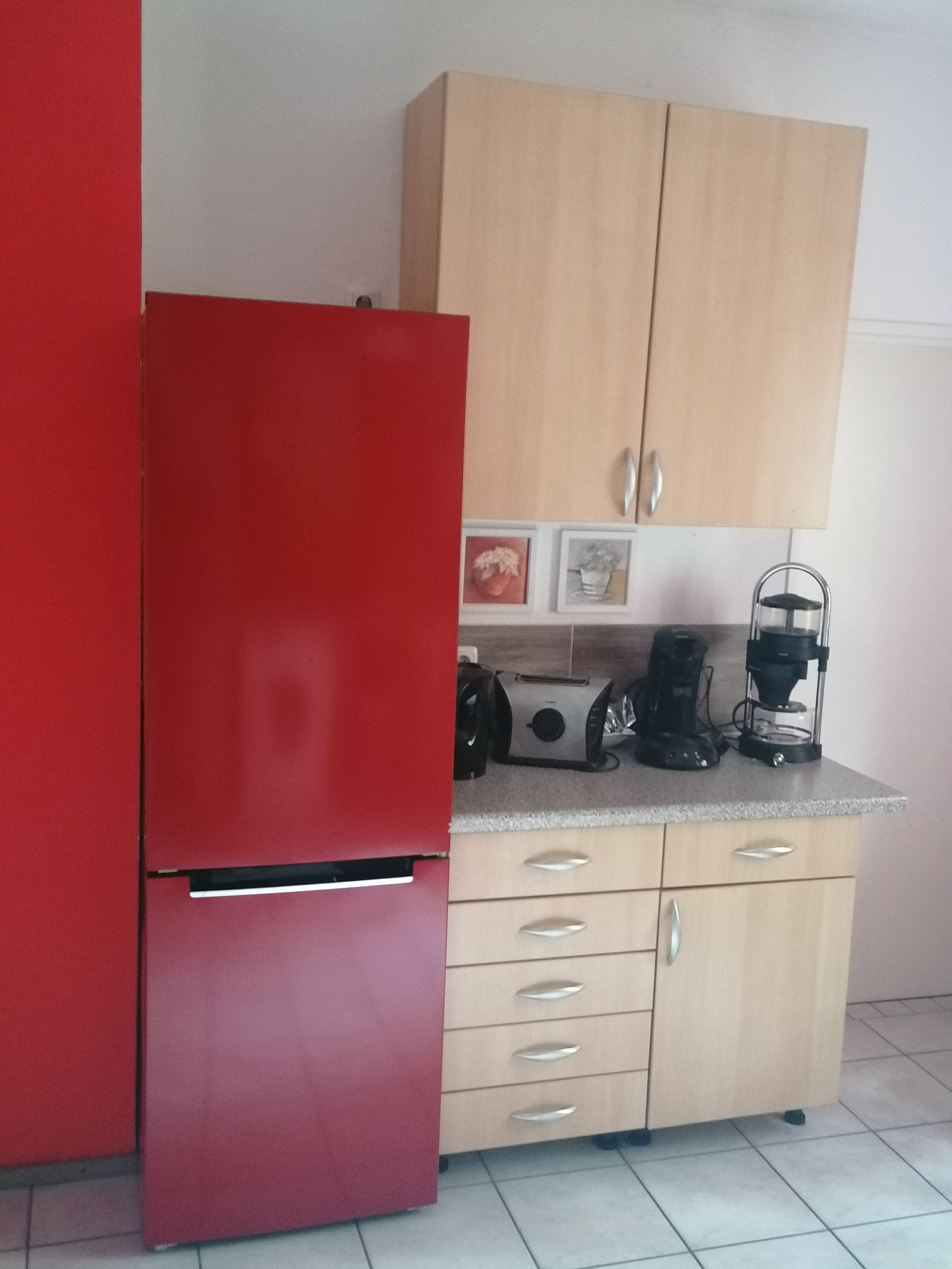 Une cuisine de taille réduite avec un réfrigérateur rouge, des placards en bois et un plan de travail sur lequel se trouvent une machine à café et un grille-pain.