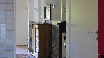 A hallway leading to a room with a wooden floor, a red door, and a clock on the wall.