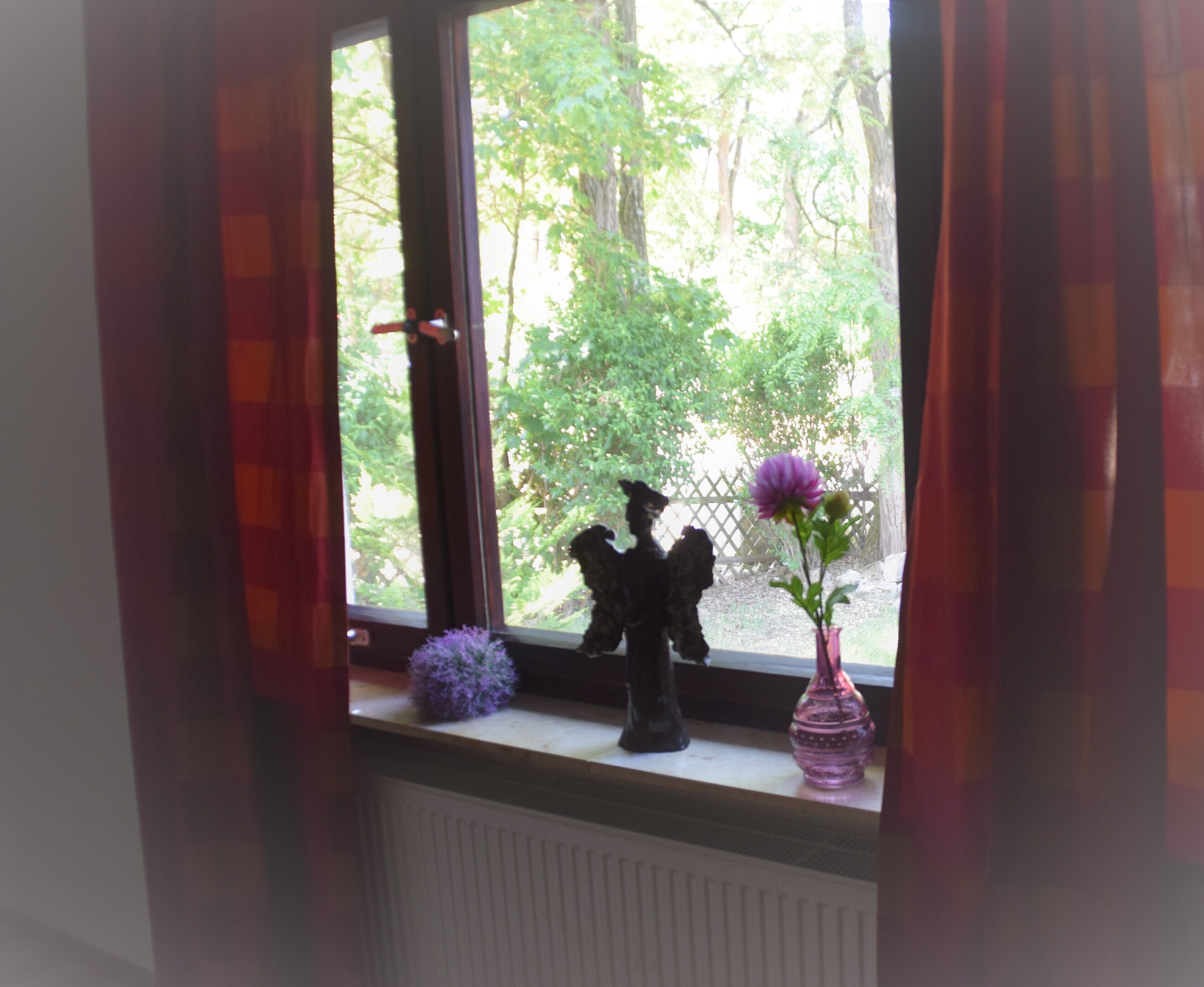 Une fenêtre donnant sur un jardin, avec une statue posée sur le rebord.