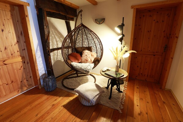 A cozy room with a hanging chair, a small table with a lamp, and a wooden floor.