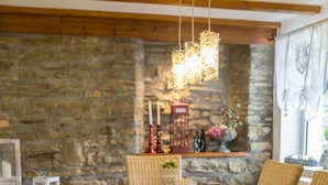 A dining area with a stone wall, wooden beams, a bench, wicker chairs, and hanging light fixtures. - 4 star holiday home "Zum Weiher" 160sqm in the heart of the Hunsrück-Hochwald National Park  (Allenbach)