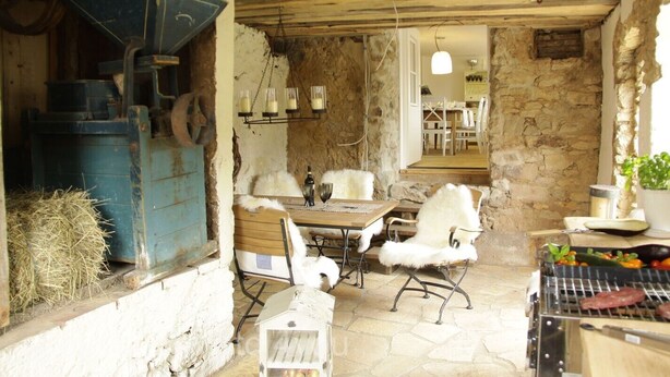 A rustic stone interior with a wooden table and chairs, a grill, and a small birdcage. - Deluxe farmhouse, smokehouse kitchen, tiled stove, bathroom in stable, Whirlpool (Bubsheim)