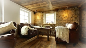 A cozy room with a stone wall, wooden ceiling, and a wooden floor. There are two leather sofas and a wooden table with a candle and a book. - Deluxe farmhouse, smokehouse kitchen, tiled stove, bathroom in stable, Whirlpool (Bubsheim)