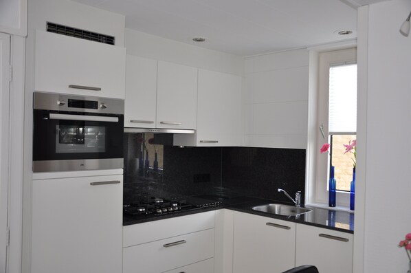 A modern kitchen with white cabinets, a black countertop, stainless steel appliances, and a window with a view.