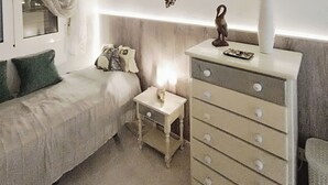 A bedroom with a bed, a dresser, a small table, a window with curtains, and wall decorations. - Top renovated holiday home with AC, Wi-Fi, satellite, infrared heating (Villamartin)