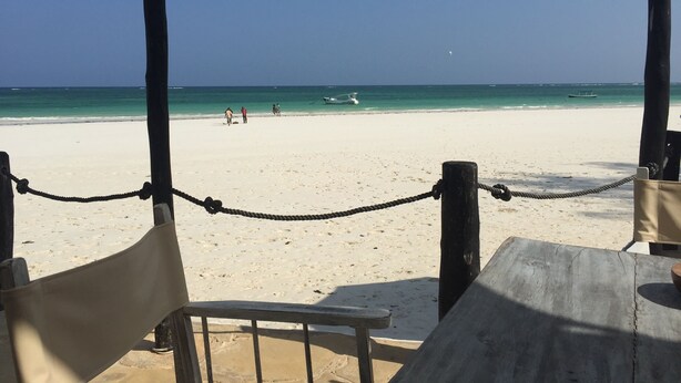 A beach view with a wooden fence and a table, and a few people in the distance.