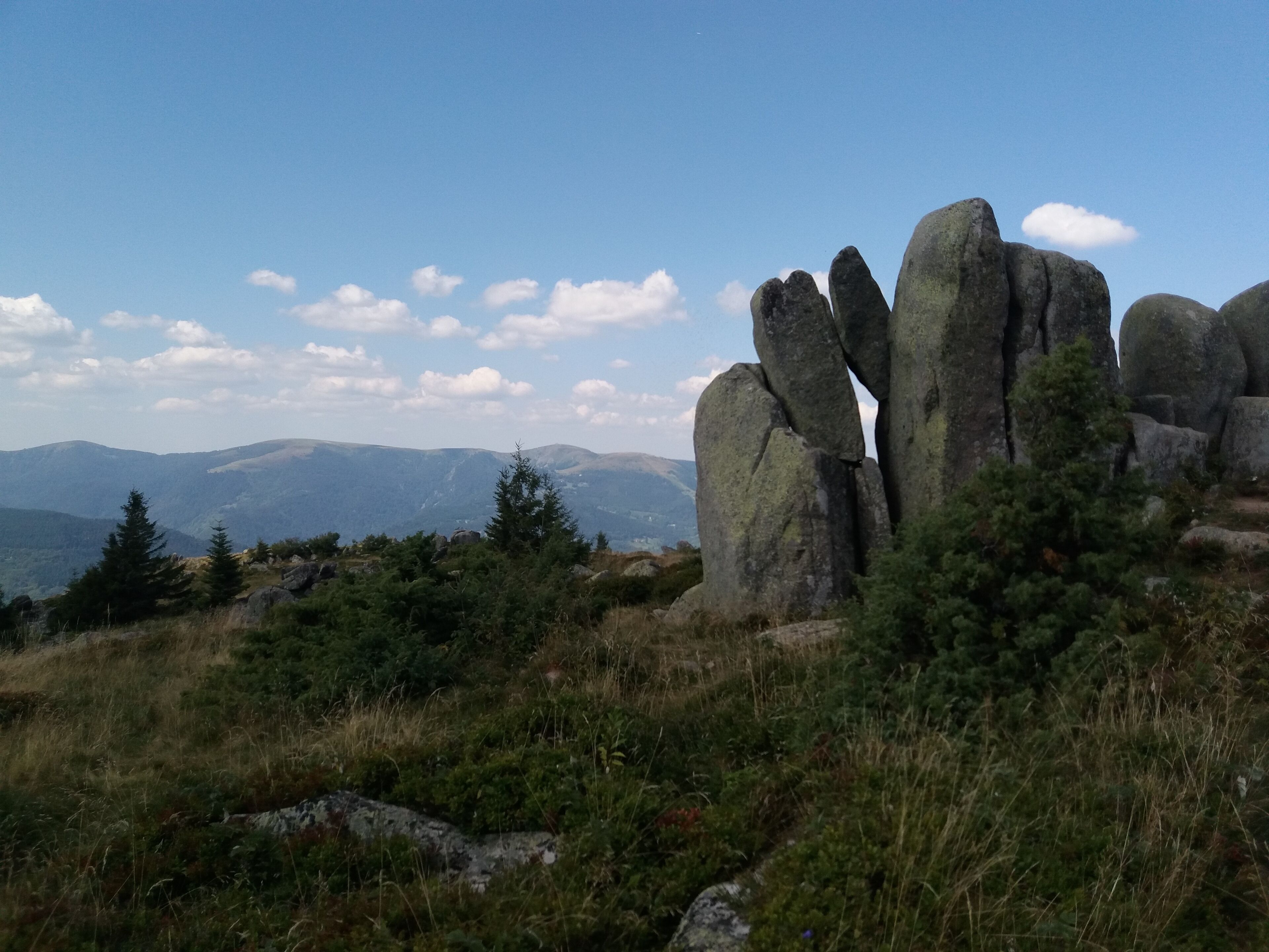 Un paysage naturel caractérisé par de gros rochers, des arbres et des montagnes lointaines, le tout sous un ciel dégagé.