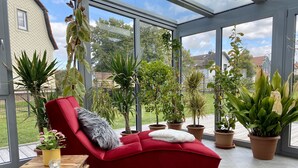 A sunlit room with a red sofa, a dog, and various potted plants. - Vacation home with pet-friendly large fenced garden in Bad Tabarz. (Tabarz/Thüringer Wald)