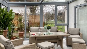A conservatory with wicker furniture, a table, and potted plants. - Vacation home with pet-friendly large fenced garden in Bad Tabarz. (Tabarz/Thüringer Wald)