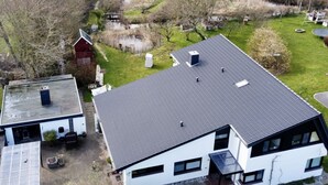 Une maison moderne avec un toit en pente, un petit étang et une grange rouge en arrière-plan.