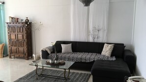 Una sala de estar con un sofá negro, una mesa de centro de cristal y un jarrón decorativo.