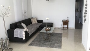 Una sala de estar moderna con un sofá negro, una mesa de centro de vidrio, un tapete gris y un jarrón decorativo con flores.