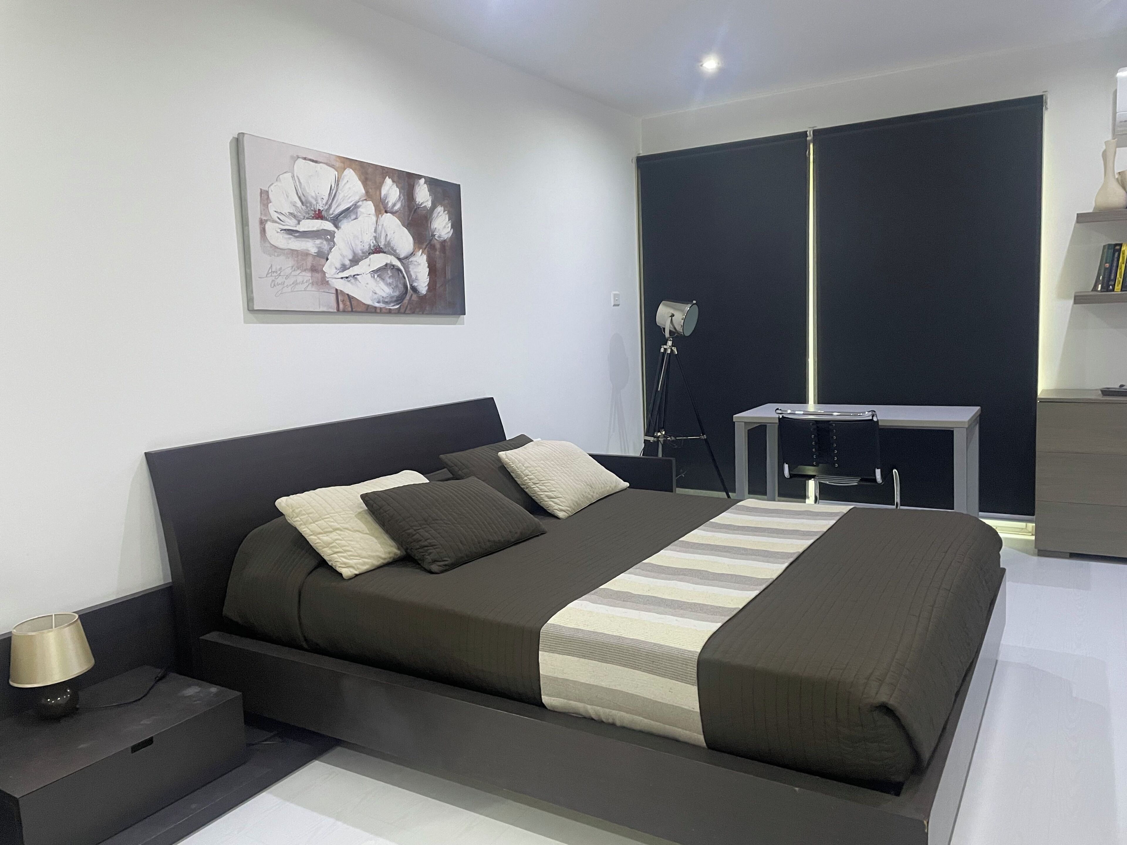 A modern bedroom with a large bed, a desk, and a wardrobe.
