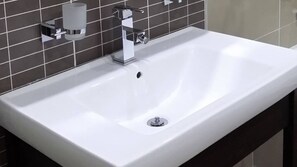 Un baño moderno con lavamanos blanco, grifo cromado y dispensador de jabón en la pared.