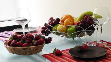 A table with a fruit basket, two wine glasses, and a plate with a strawberry.