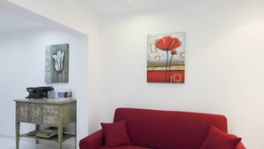 Ein Zimmer mit einer roten Couch, einer Vintage-Schreibmaschine auf einem Holzschrank und zwei Kunstwerken an den Wänden.
