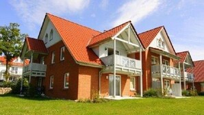 A two-story residential building with a red-tiled roof, a balcony on the upper floor, and a well-maintained lawn in front. - Newly furnished apartment with a large terrace (Ostseebad Boltenhagen)