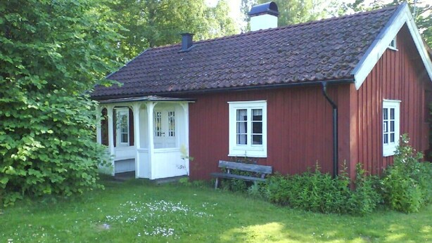 Een rode houten woning met een witte veranda en een kleine bank.