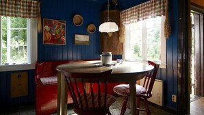 Een kamer met een houten tafel en stoelen, een rode bank en een raam met geruite gordijnen.
