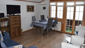 A living room with a TV, a dining table with chairs, a sofa, and a bookshelf.