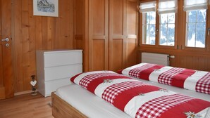 A wooden-paneled room with a bed, a dresser, and a window with a view of snow-capped mountains.