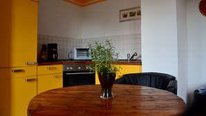 A kitchen with yellow cabinets, a wooden table, and a potted plant. - Apartment for 2 pers. with a view of Mildenstein Castle (Leisnig)