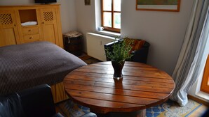 A room with a bed, a wooden table with a plant, a radiator, and a window with curtains. - Apartment for 2 pers. with a view of Mildenstein Castle (Leisnig)
