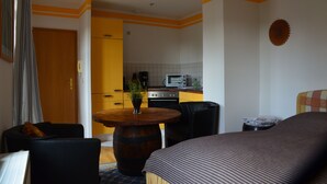 A room with a bed, a round wooden table with a plant, a sofa, and a kitchen in the background. - Apartment for 2 pers. with a view of Mildenstein Castle (Leisnig)
