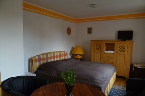 Ein Hotelzimmer mit einem Bett, einem Holzschrank, einem Fernseher, einer Lampe, einem Sessel und einem kleinen Tisch mit einer Pflanze.