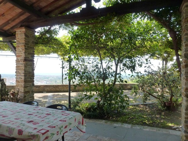 An outdoor seating area with a table covered in a floral tablecloth, stone pillars, and a view of the cityscape.