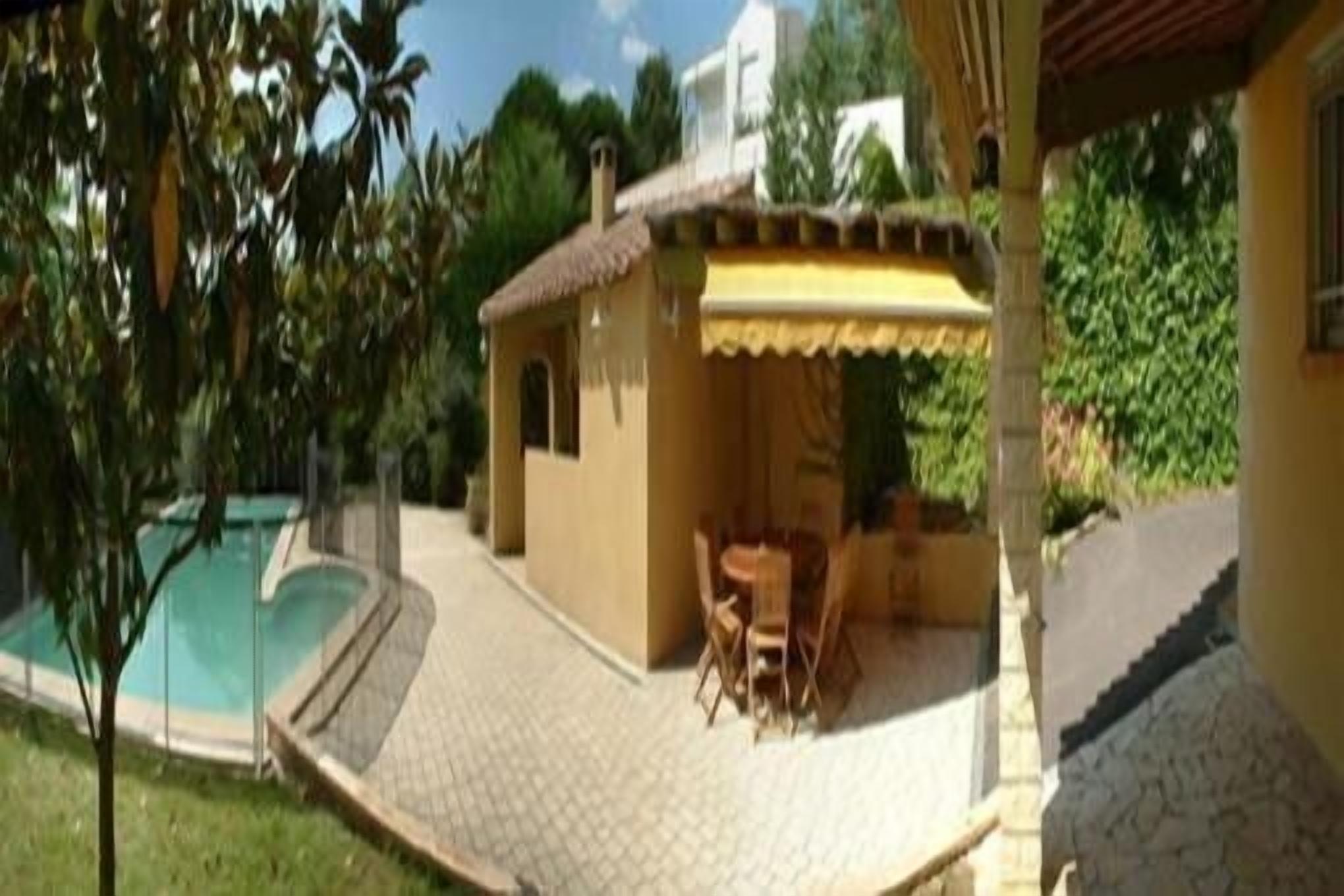 Une maison avec une piscine, un patio avec une table et des chaises, et un espace couvert doté d’un auvent jaune.