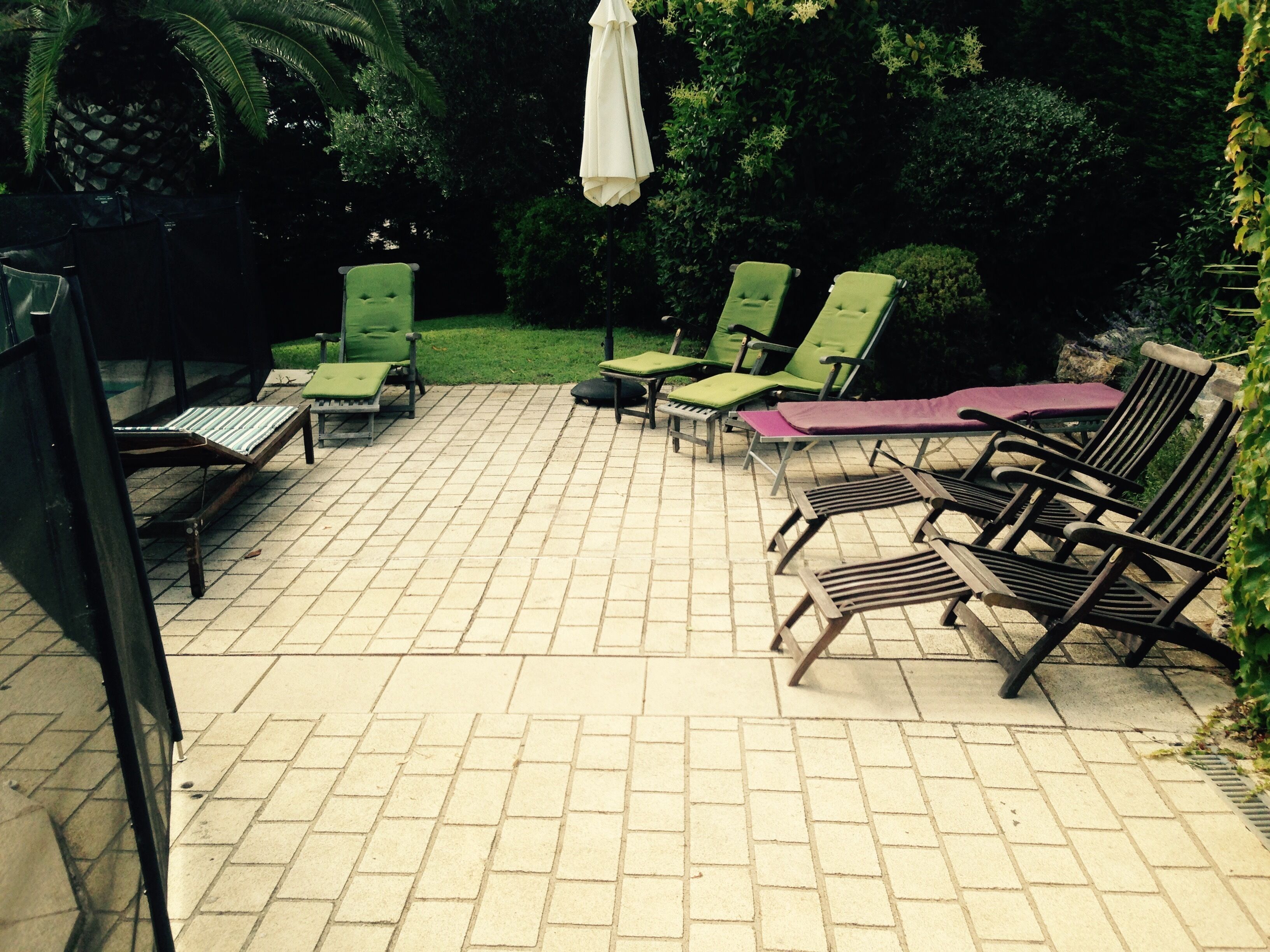 Un espace extérieur aménagé en patio, doté d’un sol carrelé et de plusieurs fauteuils de relaxation, dont certains sont pourvus de coussins.