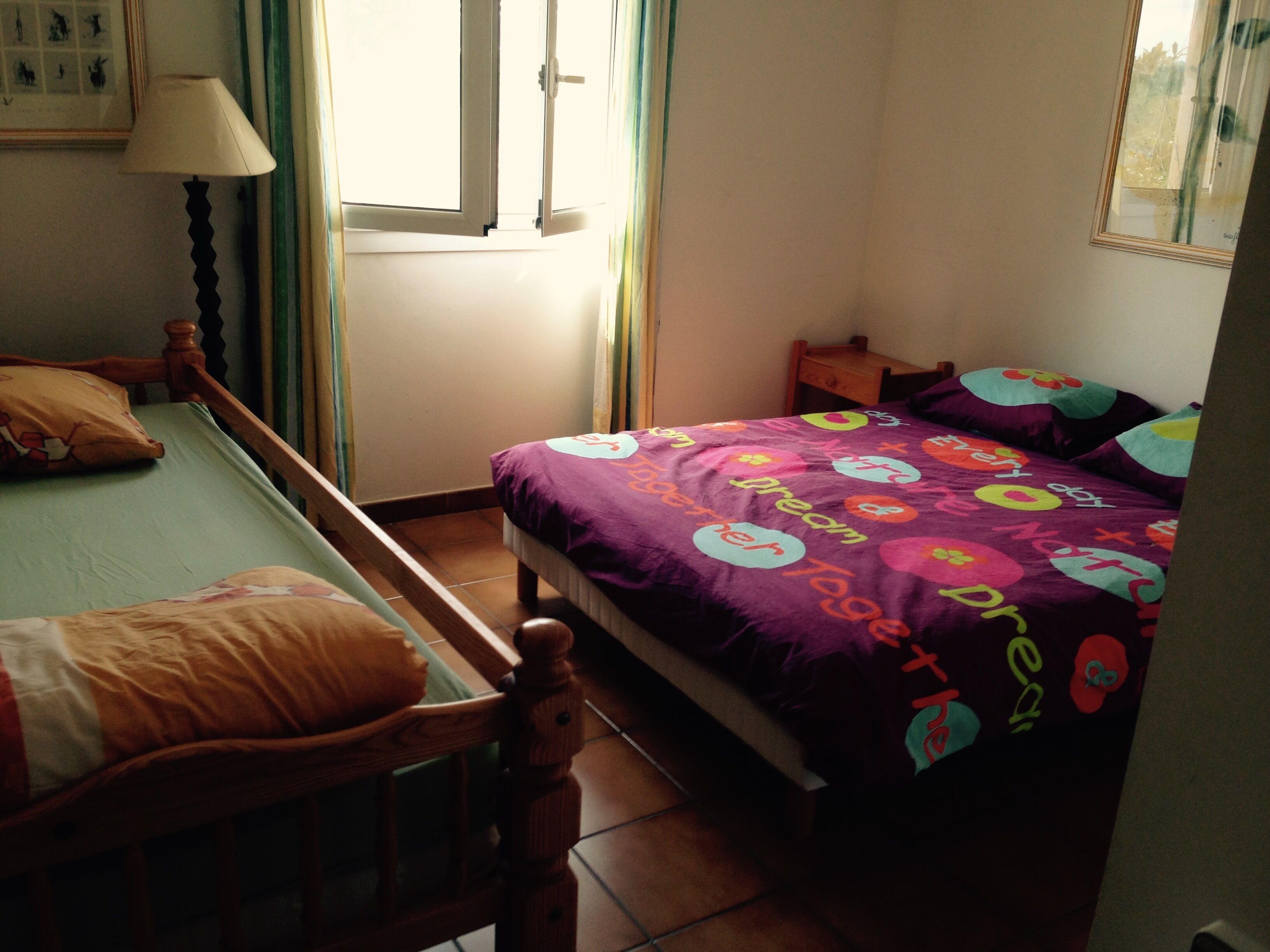 A bedroom with a bed, a chair, a window, and a lamp.