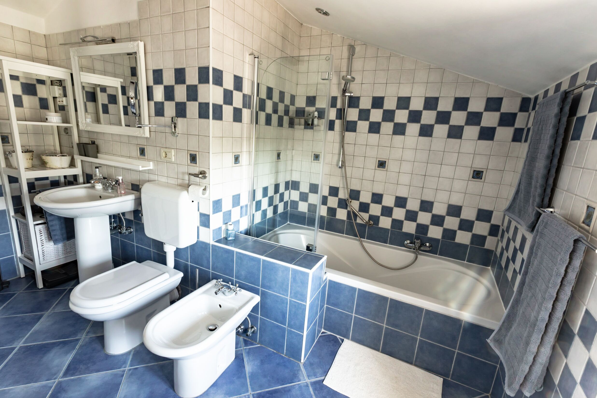 Une salle de bain avec un carrelage à motifs à carreaux, une baignoire, deux toilettes, un lavabo et un miroir.