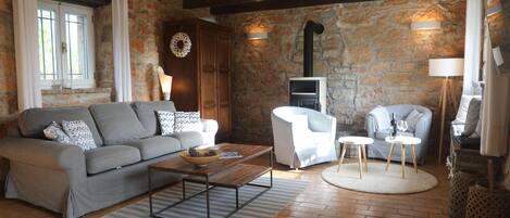 A cozy living room with a stone wall, a fireplace, a sofa, a coffee table, and a white armchair.