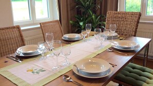 A dining table set with plates, glasses, and cutlery, surrounded by wicker chairs and a green cushioned chair. - Welcome to the Allgäu family Berger (Sulzberg)